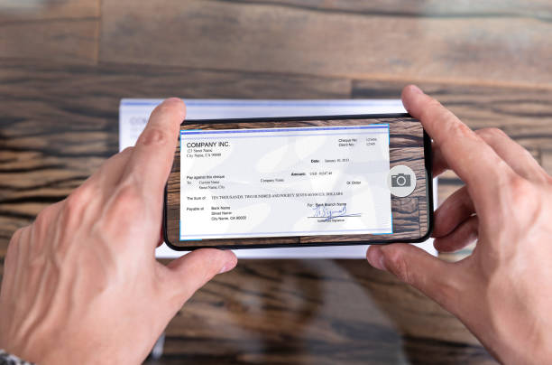 Man Taking Photo Of Cheque To Make Remote Deposit Man Taking Photo Of Cheque To Make Remote Deposit In bank wages photos stock pictures, royalty-free photos & images