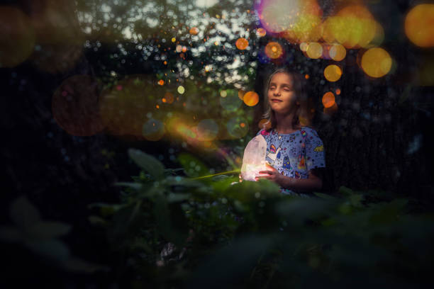 A happy little girl in a forest holding glowing crystal in her hands.