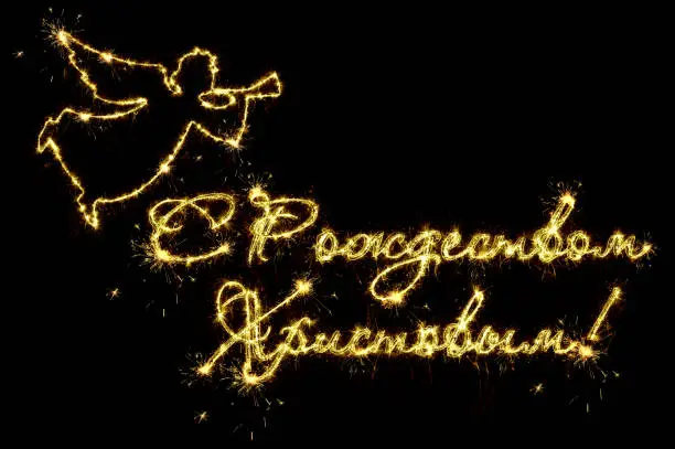 Photo of Merry Christmas text in russian. Text Merry Christmas in russian and flying angel written sparkling sparklers fireworks isolated on black background. Overlay template for christmas greeting card