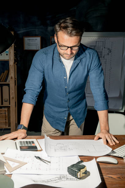istock Mature engineer in casualwear looking at sketch on paper while working overtime 1186385675