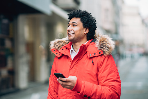 Young african american man walking on the street with red jacket and smart phone