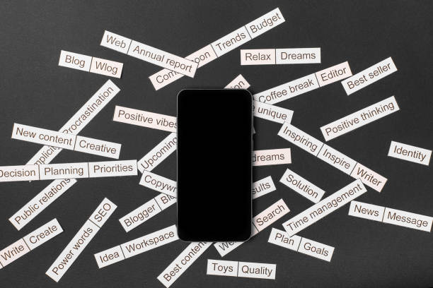 Smartphone surrounded by a cloud of words on business themes cut out of paper on a gray background Smartphone surrounded by a cloud of words on business themes cut out of paper on a gray background, strategic themes stock pictures, royalty-free photos & images