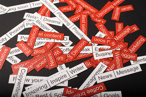 Word cloud of business themes cut out of red and white paper on a gray background.