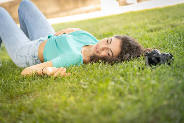 fille de photographe se trouvant sur l'herbe heureuse et souriante, détendant - attractive female square looking at camera outdoors photos et images de collection