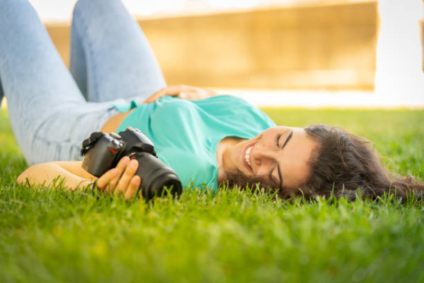 fille de photographe se trouvant sur l'herbe heureuse et souriante, détendant - attractive female square looking at camera outdoors photos et images de collection