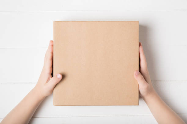 istock Square cardboard box in children hands. Top view, white background 1186396400