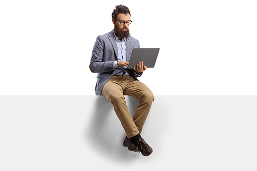 Chico barbudo con en un ordenador portátil sentado en un panel photo