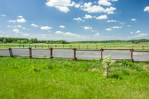 Parking in nature with a wooden fence, trees on the horizon and white clouds on a blue sky. Czarnolas, Poland.