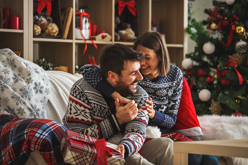 Young couple hugging and laughing while relaxing at home on Christmas day.