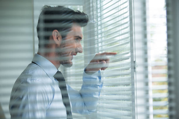 istock Curious man peeking through window shades 1186414754