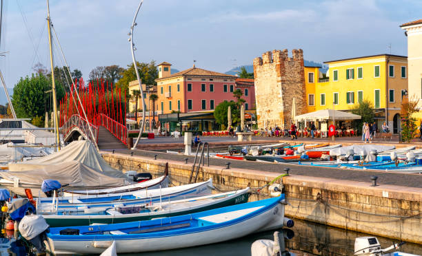 Boats in old town port of Bardolino and tourists walking and sitting in restaurants. The town is a popular holiday destination in Garda Lake district. stock photo