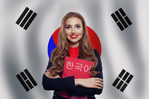 Study korean language. Happy cheerful woman student on the Republic of Korea flag background. Korean language school concept. Book with inscription Korean on korean language