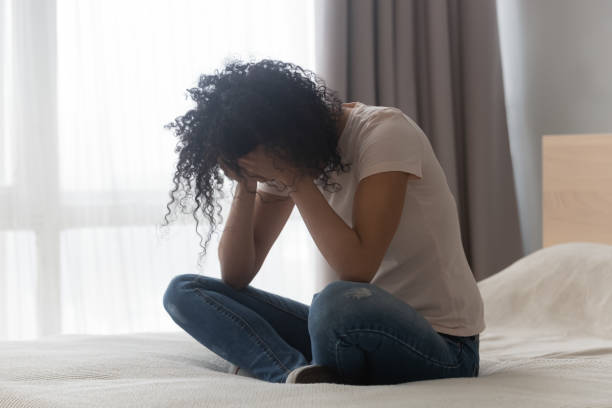przygnębiona afrykańska kobieta siedząca samotnie w łóżku - women crying distraught thinking zdjęcia i obrazy z banku zdjęć