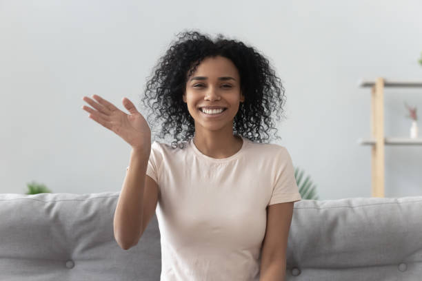 African woman feels happy wave hand looking at camera Happy african woman sit on couch wave hand looks at camera make video call use computer webcam view, instant virtual chat online communication, vlogger record webinar, job interview distantly concept divergent movie review stock pictures, royalty-free photos & images