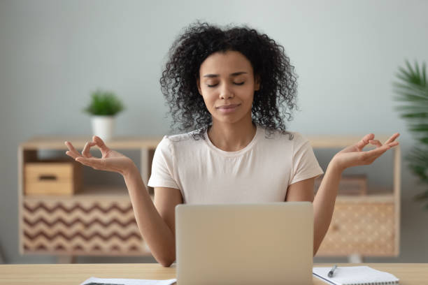 mujer africana meditando sentada en el escritorio frente a la computadora portátil - career break fotografías e imágenes de stock