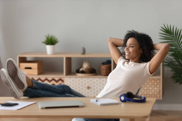 mujer pone las manos detrás de las piernas de la cabeza en el escritorio relajante en el interior - career break fotografías e imágenes de stock