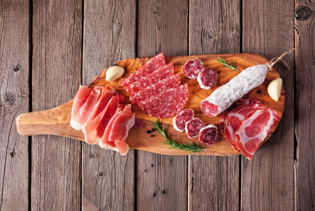 Meat appetizer platter with sausage, prosciutto, ham and salami, top view on a serving board against wood Meat appetizer platter with sausage, prosciutto, ham and salami. Top view on a serving board against a wood background. appetizer plate stock pictures, royalty-free photos & images