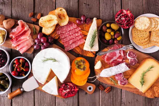 Charcuterie boards of assorted meats, cheeses and appetizers. Top view table scene on a rustic wood background.