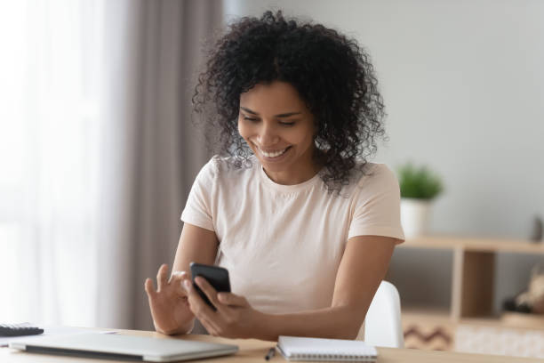 istock Positive african woman sit at desk typing message using smartphone 1186425308