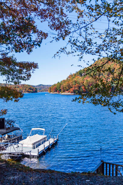 Colorful autumn leaves and pontoon boats moored at a dock on a pond near the North Carolina Appalachians Colorful autumn leaves and pontoon boats moored at a dock on a pond near the North Carolina Appalachians pontoon boat stock pictures, royalty-free photos & images