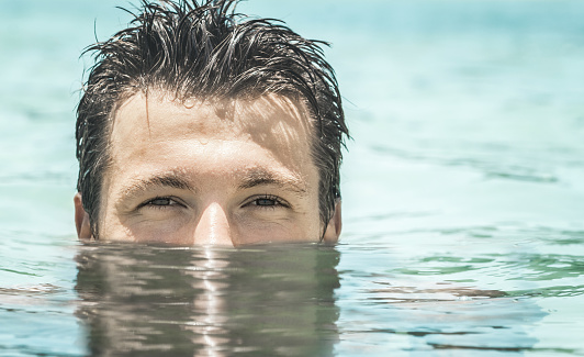 Attractive young man  swimming in the azure sea with half face submerged underwater