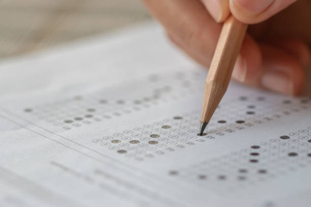 istock Exam test school or university concept : Hand student holding pencil writing standardized answer multiple carbon paper form with gray black answers sheet bubbled doing final assessment in classroom 1186454349