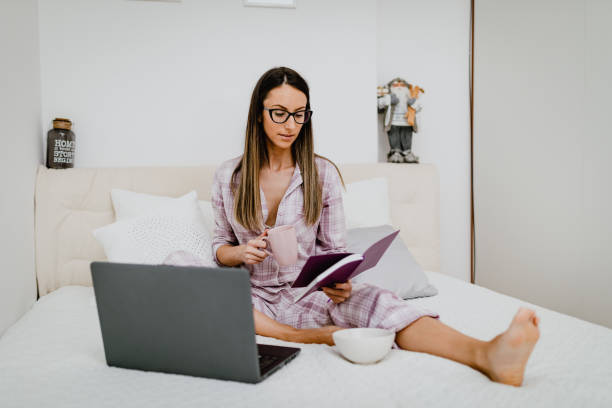 istock Woman in pajamas drinking coffee and using laptop in bed 1186465967