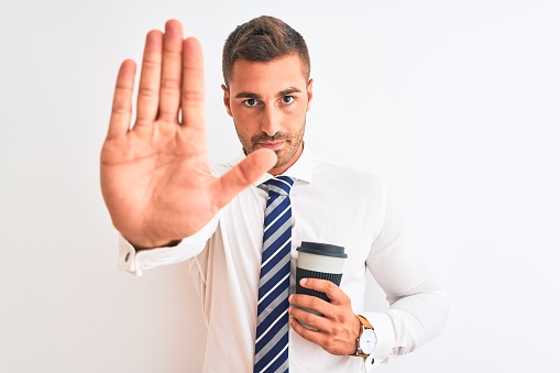 Young handsome business man drinking take away coffee over isolated background with open hand doing stop sign with serious and confident expression, defense gesture