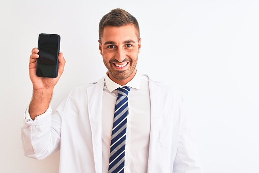 Young scientist man showing smartphone screen over isolated background with a happy face standing and smiling with a confident smile showing teeth