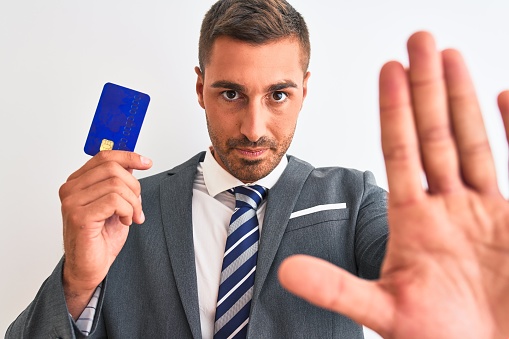 Young handsome business man holding credit card over isolated background with open hand doing stop sign with serious and confident expression, defense gesture