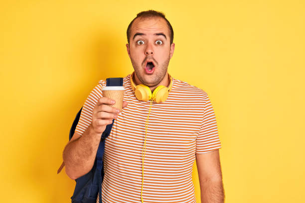 istock Student man wearing backpack headphones drinking coffee over isolated yellow background scared in shock with a surprise face, afraid and excited with fear expression 1186467630