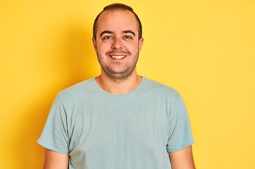 Young man wearing green casual t-shirt standing over isolated yellow background with a happy and cool smile on face. Lucky person.