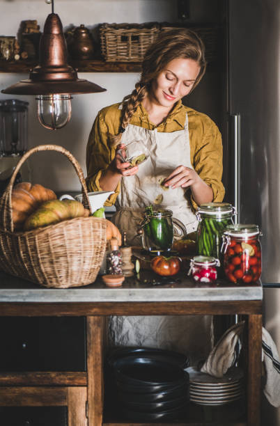 junge blonde frau in leinen schürze machen hausgemachte gemüsekonserven - rustic domestic kitchen canning vegetable stock-fotos und bilder