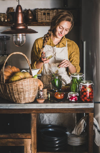リネンエプロンの若いブロンドの女性は、自家製の野菜の保存を作ります - canning ストックフォトと画像