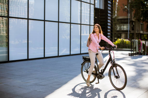 Young woman riding an electric bicycle Young woman riding an electric bicycle in urban environment electric bicycle photos stock pictures, royalty-free photos & images