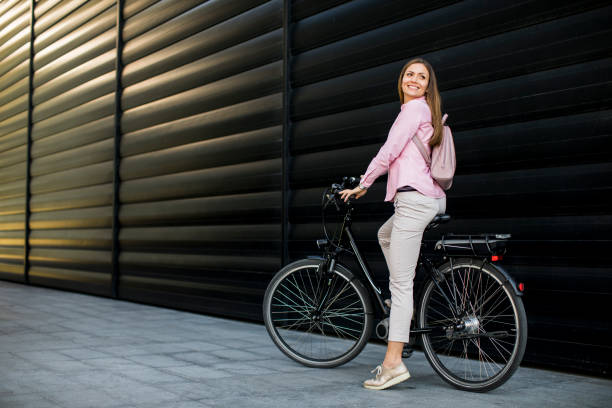 jeune femme avec l'e-bike électrique moderne de ville comme transport urbain propre et durable - city bike photos et images de collection