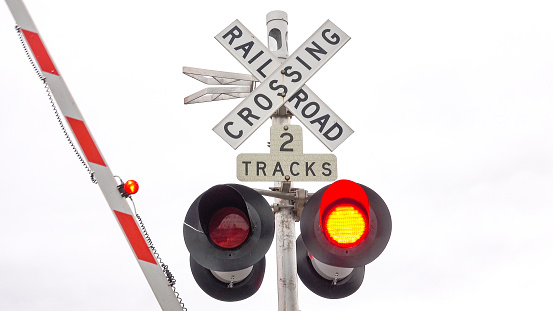 CLOSE UP: Isolated railroad crossing traffic sign with flashing red lights and barrier lowering indicating that a train is coming. Traffic symbols on a intersection of a car road and a railway tracks