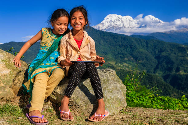 Happy Nepali little girls using digital tablet, Annapurna Range on background. The Annapurna region is in western Nepal where some of the most popular treks (Annapurna Sanctuary Trek, Annapurna Circuit) are located. Peaks in the Annapurnas include 8,091m Annapurna I, Nilgiri and Machhapuchchhre. The Annapurna peaks are among the world's most dangerous mountains to climb.