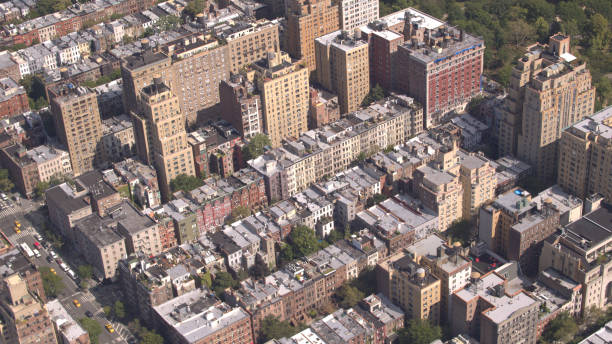 AERIAL: Flying above Upper West side overlooking green Central park in New York AERIAL: Flying above Upper West side overlooking lush green Central Park in sunny New York City. Luxury condominium apartment buildings with Central Park view along the busy avenue full of yellow cabs columbus avenue stock pictures, royalty-free photos & images