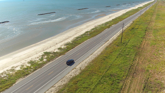AERIAL: Black SUV car driving on countryside road along the Bay of Mexico. People traveling, road trip on empty road through beautiful countryside scenery in sunny summer