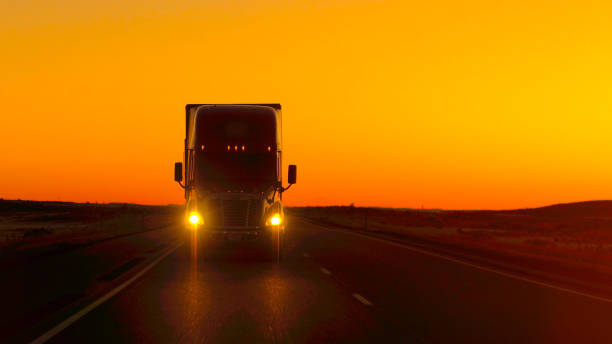 CLOSE UP LENS FLARE: Semi truck driving directly into camera at golden sunset CLOSE UP LENS FLARE: Semi truck driving and hauling goods on empty highway across the Great Plains in golden morning. Freight delivery truck transporting cargo on interstate freeway at stunning sunset grassland in morning sunrise stock pictures, royalty-free photos & images
