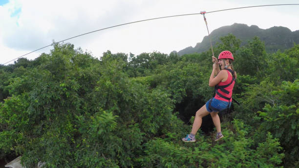 Young girl smiling and screaming when zipling on cable above lush rainforest