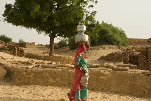 Jaisalmer, Rajasthan, India - August 19, 2011: Rajasthani carrying water jars in the head in a village along the Ramgarh Road
