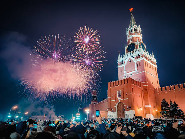 new year's eve in moscow. fireworks on red square near the spasskaya tower on new year's eve. multicolored salute in the kremlin. a large crowd of people celebrates the new year on red square. many unrecognizable people gathered for a universal celebratio - large group of people flash imagens e fotografias de stock
