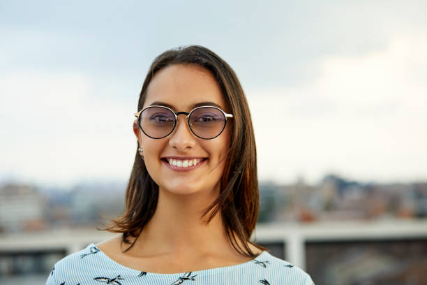 Portrait of beautiful businesswoman smiling against sky. Young female professional is wearing sunglasses. She is standing at rooftop.
