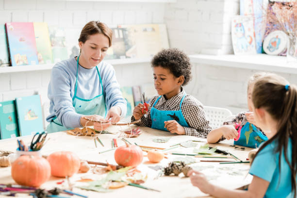 istock Young teacher pointing at stick with several halloween decorations at lesson 1186533683