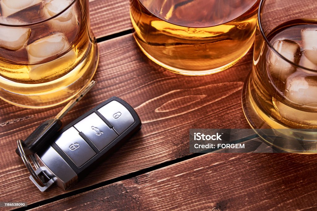 Still life on old wooden table top. Car keys, several glasses and a bottle of whiskey or alcohol. Suitable for drunk driving. Drinking Stock Photo