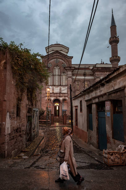 Ayvalik, Turkey - October 22, 2015: A woman walks down a street on a rainy evening in Ayvalik, Turkey. In the background is the Cinarli Mosque. The building was a church until the founding of the Turkish Republic after World War I.