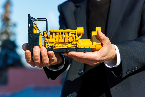 A toy model of a gas generator set is in the male hand. Selective focus.