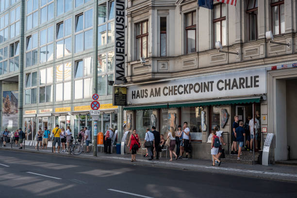 People stand on a sidewalk outside Haus Am Checkpoint Charlie, a private museum in Berlin, Germany.  Checkpoint Charlie was the main crossing point at the Berlin Wall between West Berlin and East Berlin during the Cold War.